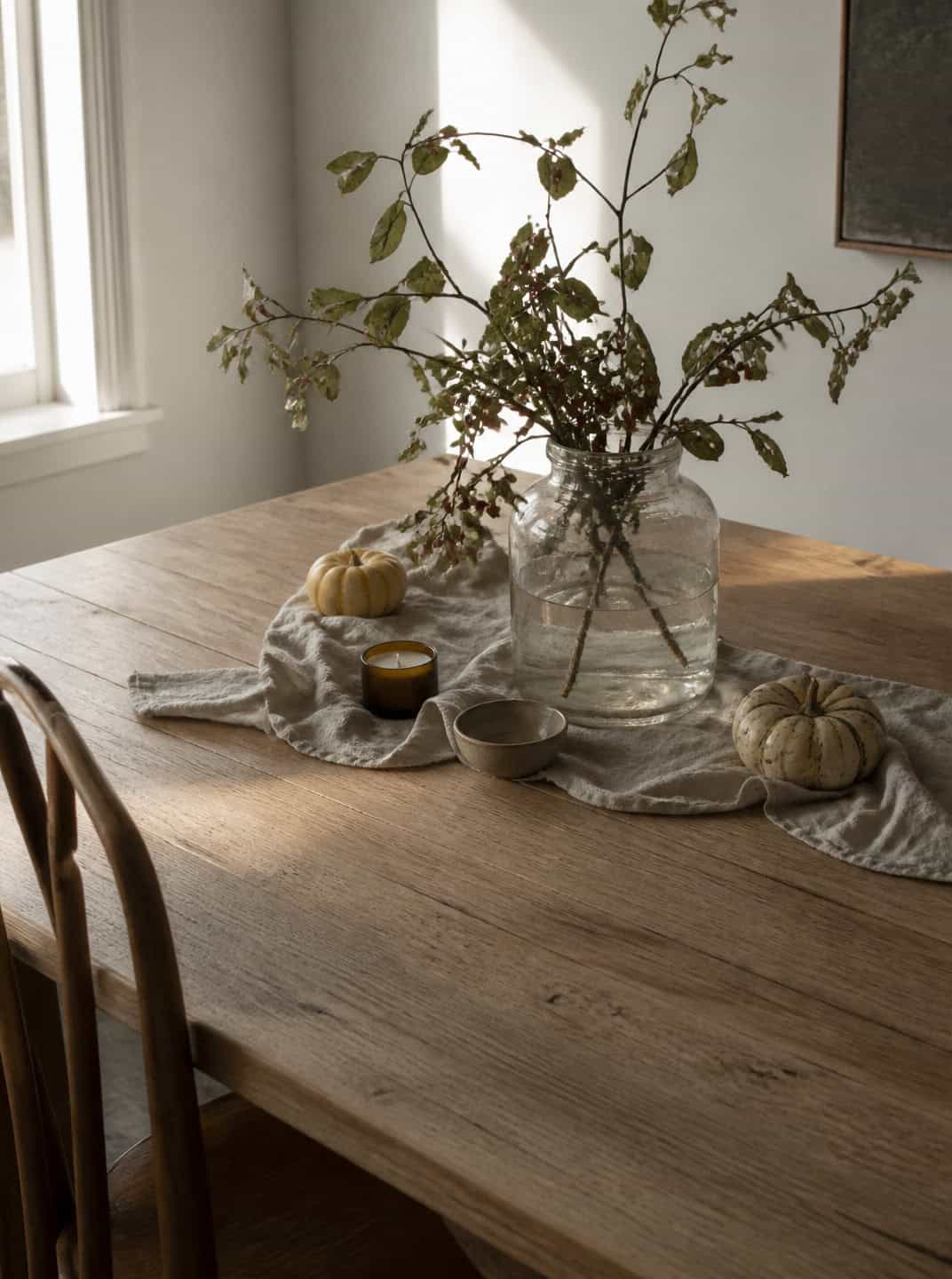 Rustic table with pumpkins, candle, and fall branches: Halloween centerpiece idea.