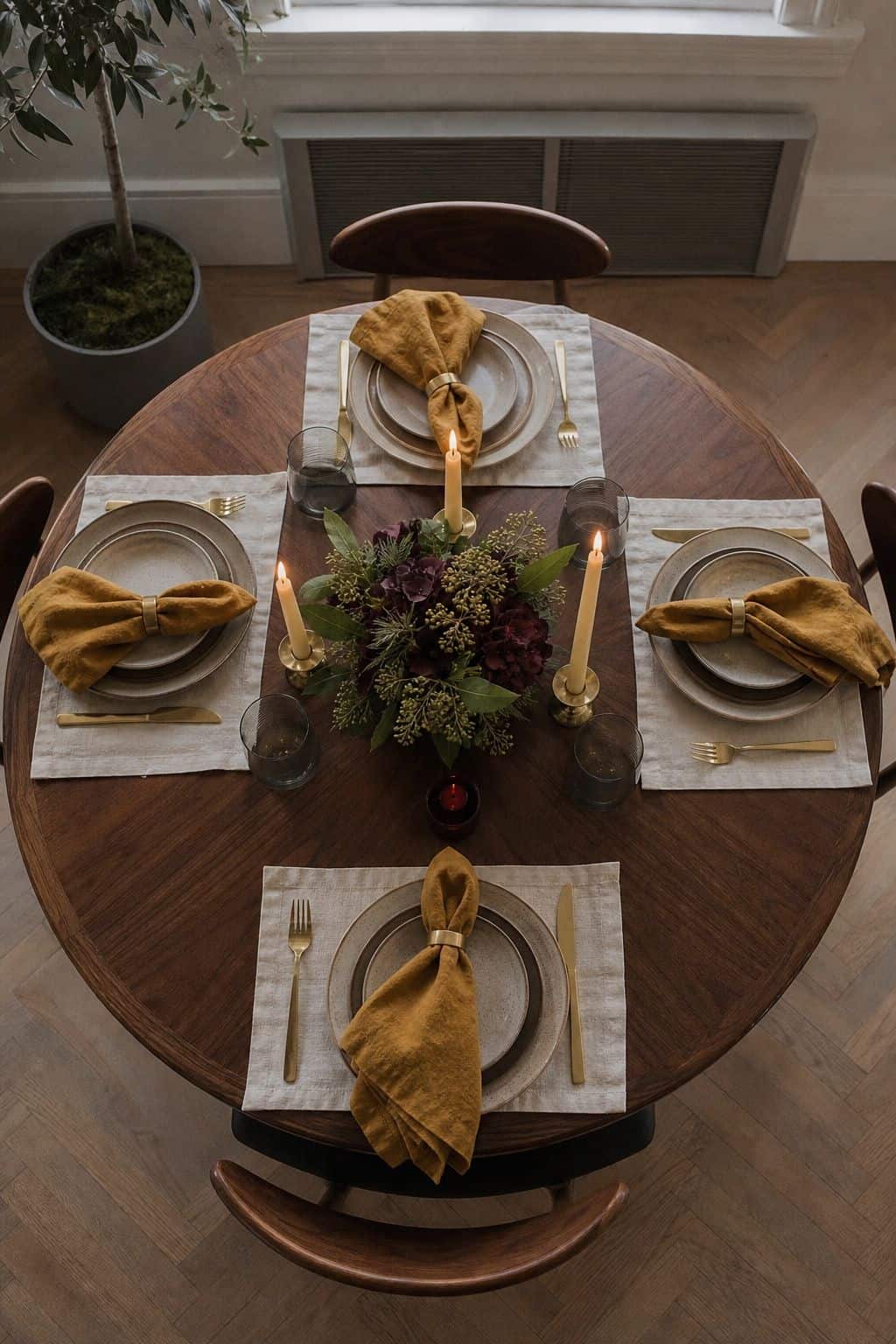 Round Thanksgiving table with four equal-height candles around a low centerpiece and mustard napkins