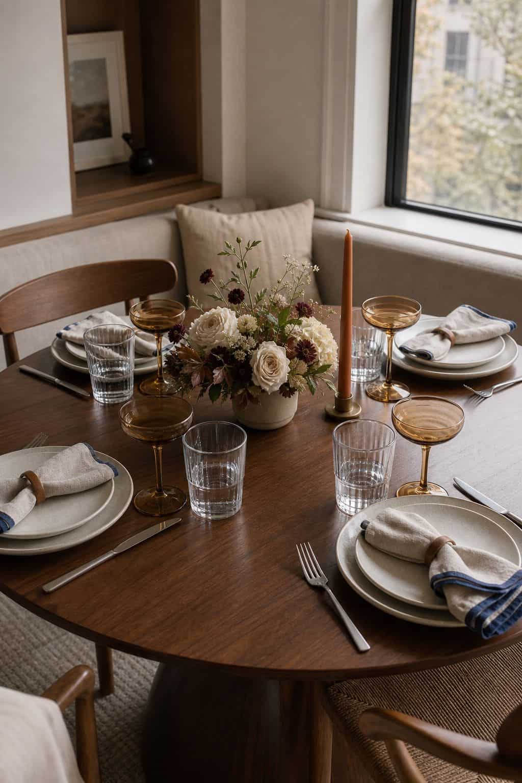 Round Thanksgiving table with water glasses, amber coupe glasses, low centerpiece, and deep blue accents