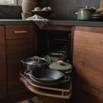Deep corner kitchen cabinet with pull-out shelves, cookware, lids, and a muted green pot