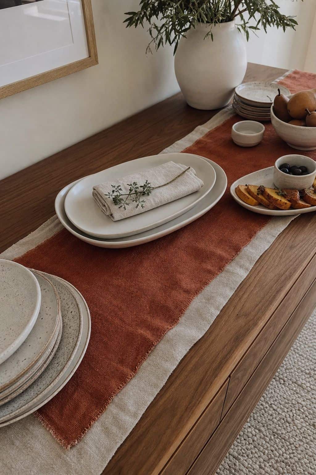 Layered oatmeal and terracotta linen runner under Thanksgiving buffet dishes on a walnut table