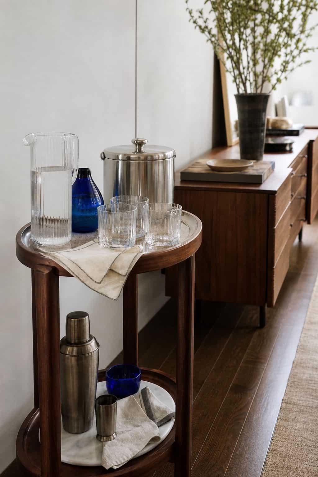 Small self-serve drink station with glass pitcher, tumblers, and deep blue accents near a buffet