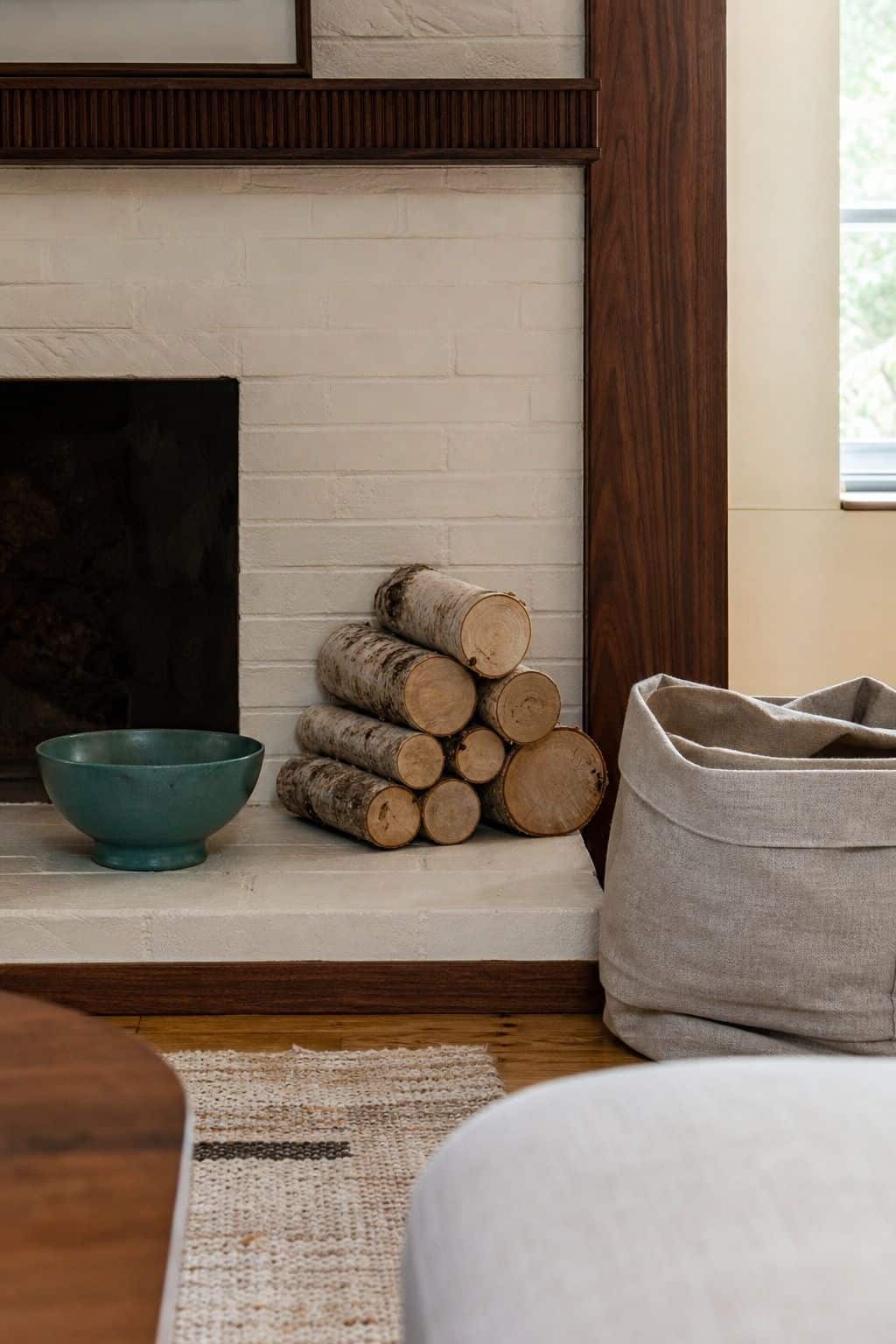 Birch logs stacked beside a fireplace opening with a muted green accent bowl