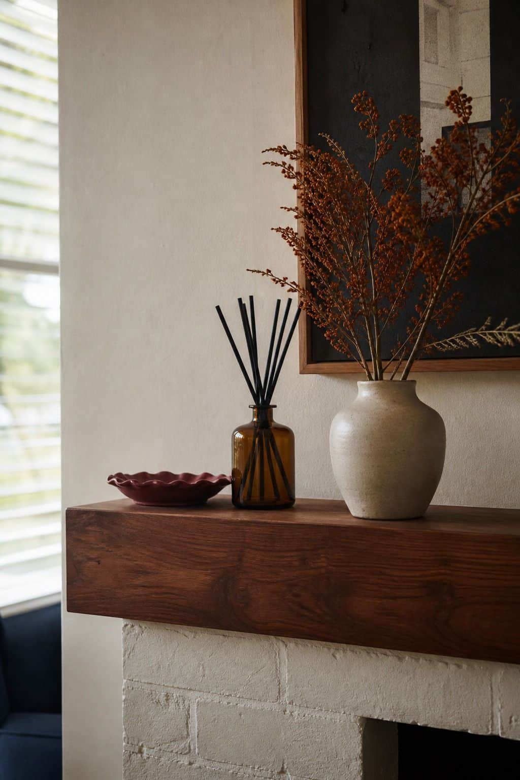 Amber reed diffuser on a walnut mantel with dried stems for Thanksgiving decor