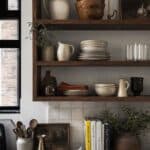 Open shelves with walnut bowls, cream ceramics, stoneware stacks, and a rust linen accent.